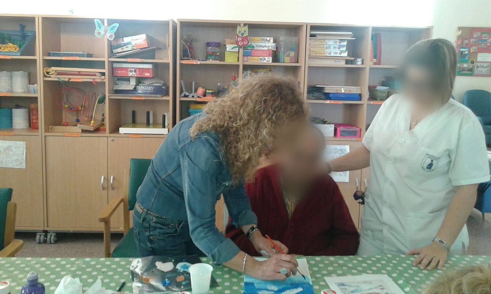 Profesora pintando un cielo azul junto a un usuario y una cuidadora del Centro de Día