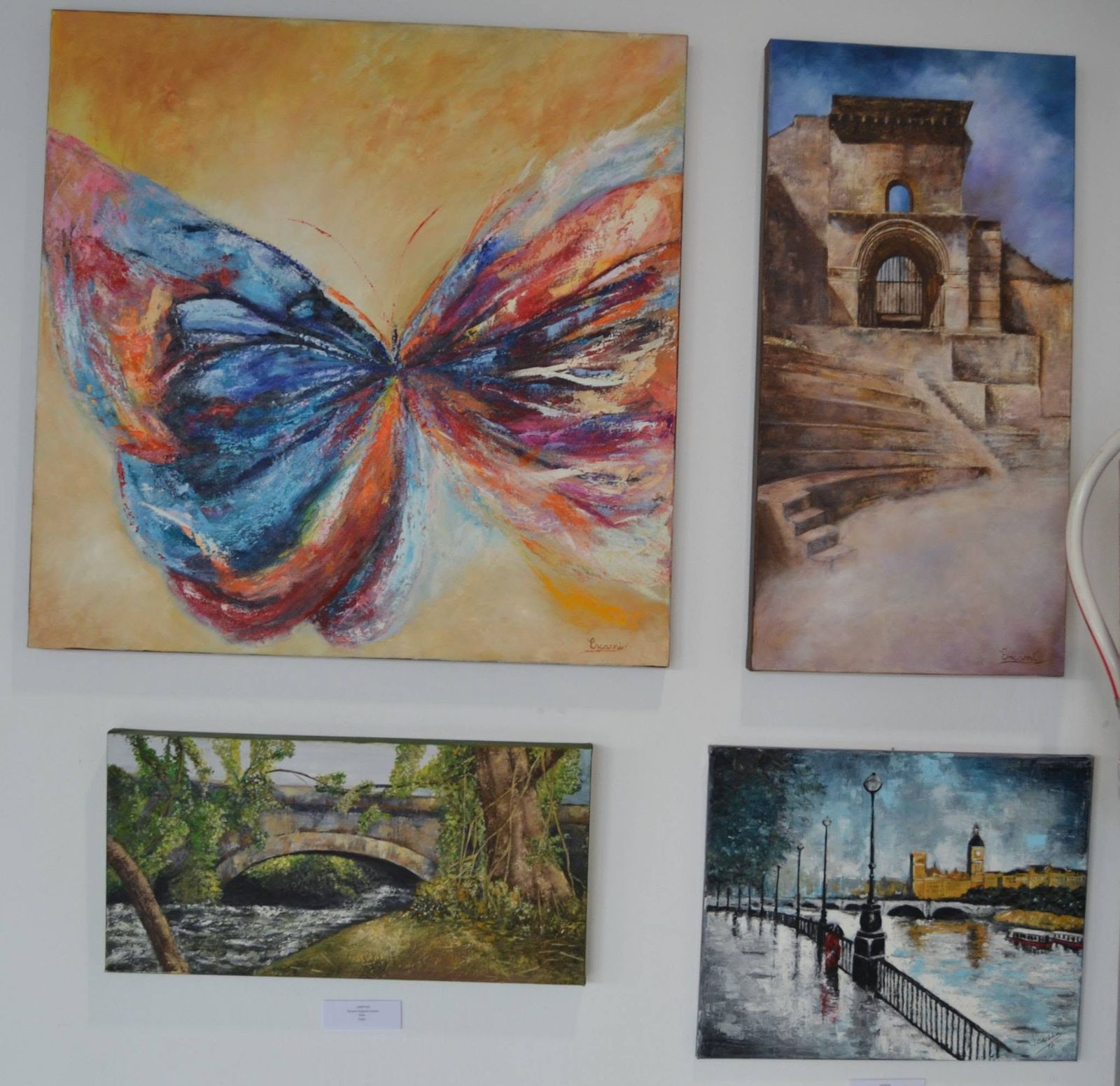 Cuadros expuestos en el Luzzy: mariposa multicolor, edificio histórico y escenas urbanas