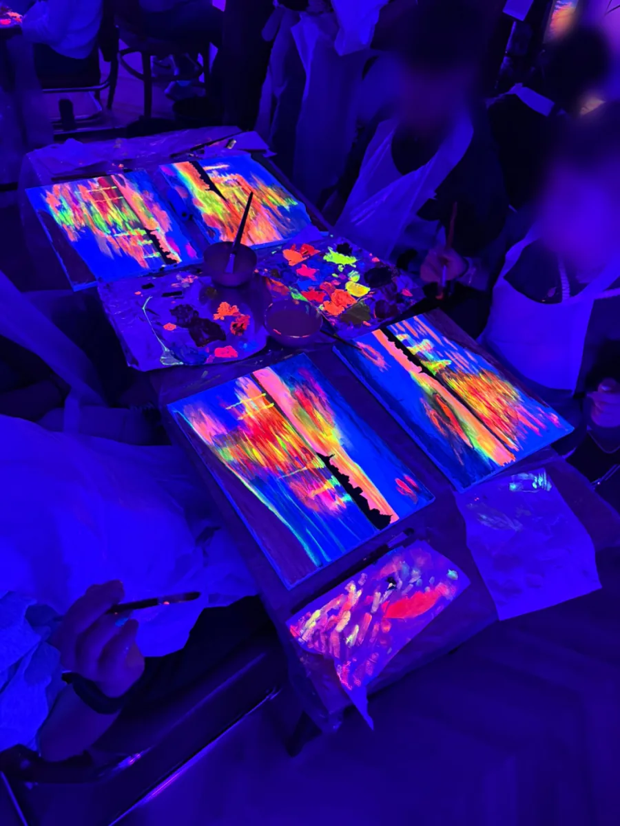 Participantes pintando con colores neón alrededor de una mesa bajo luz ultravioleta