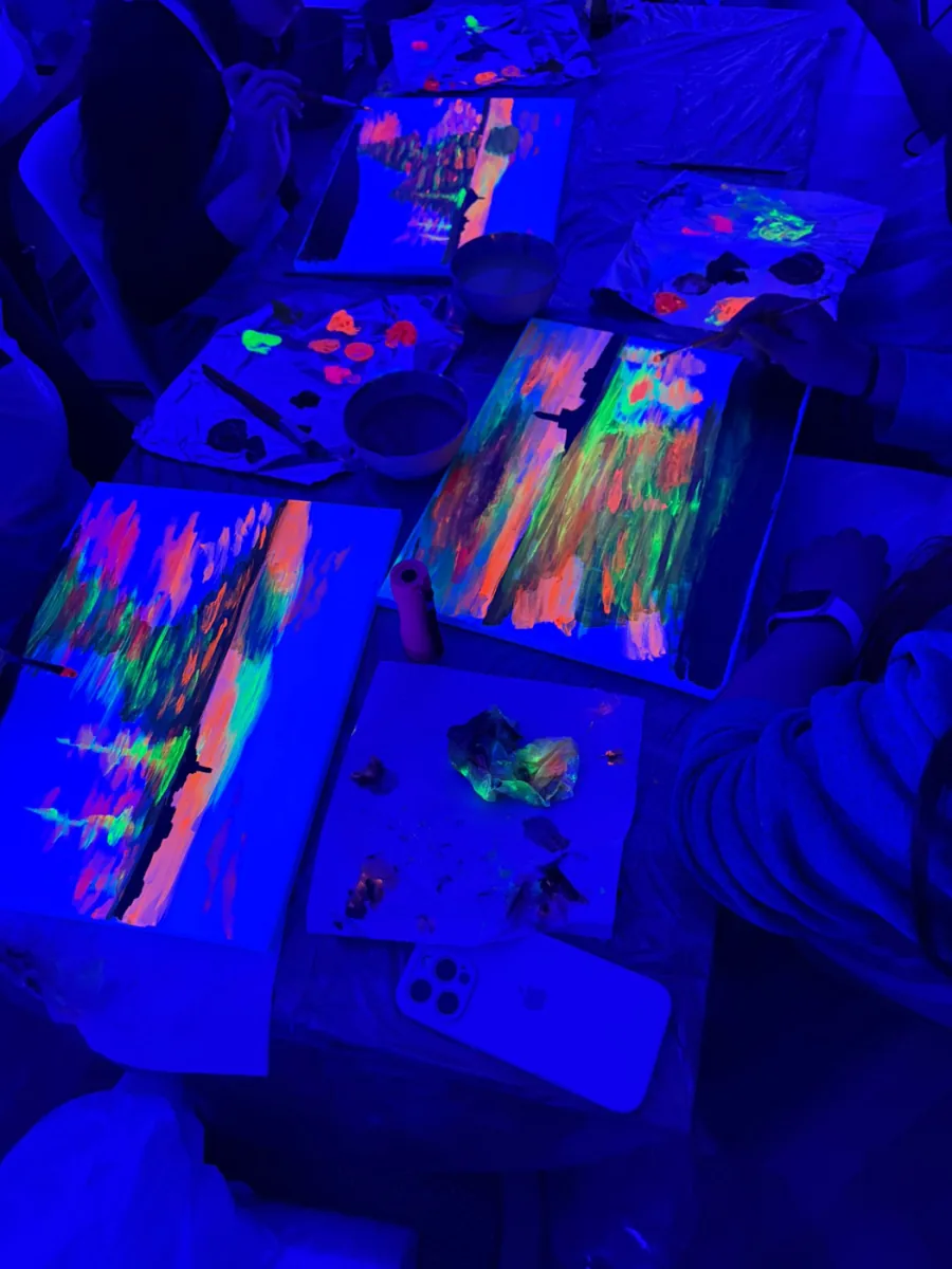 Mesa con lienzos y paletas de pintura fluorescente durante un taller de neón